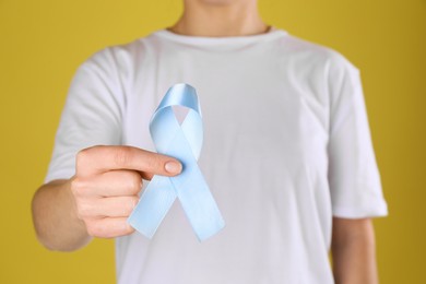 Photo of International Psoriasis Day. Woman with light blue ribbon as symbol of support on yellow background, closeup