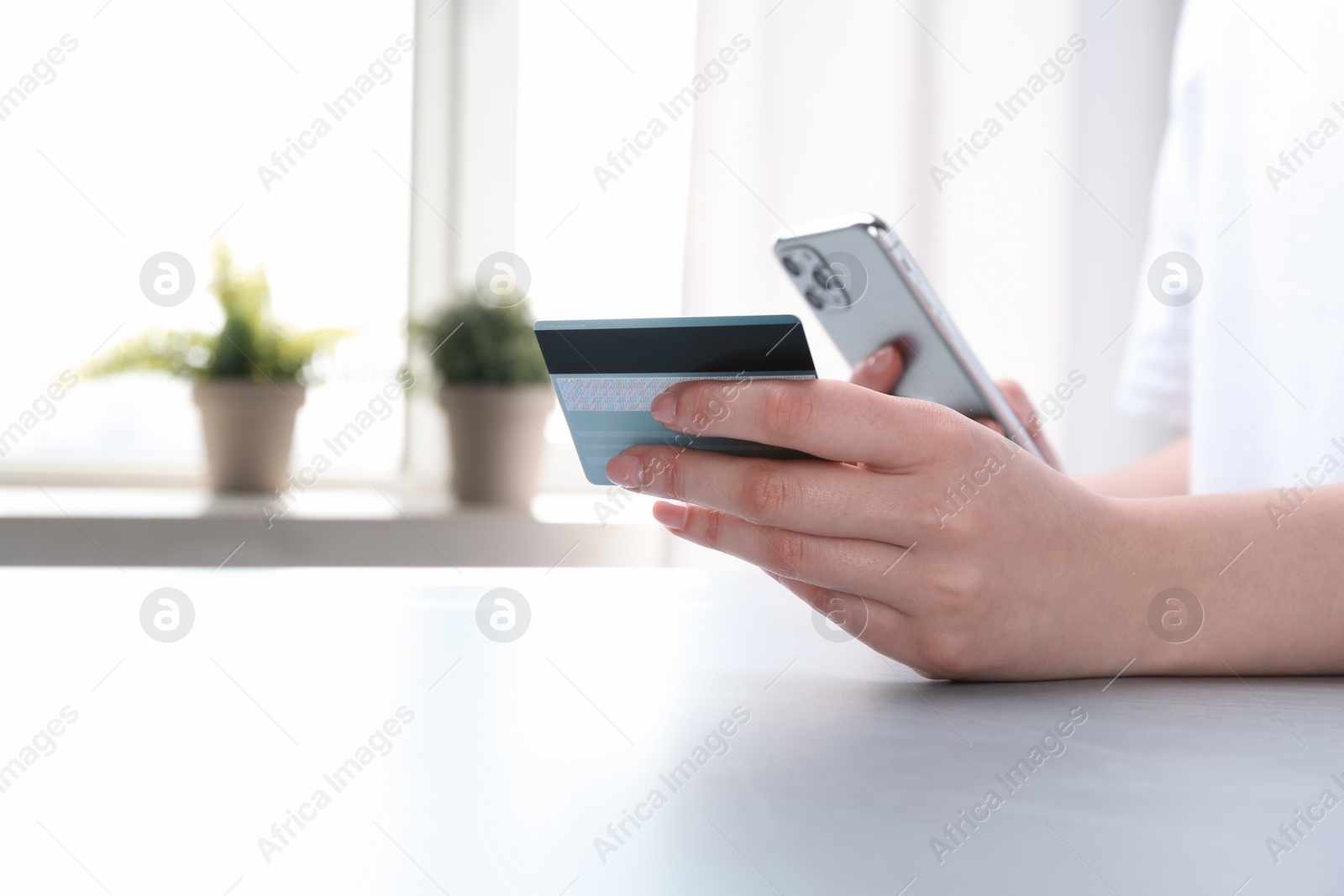 Photo of Online payment. Woman with smartphone and credit card at white table, closeup