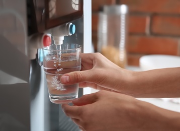 Woman filling glass with water from cooler indoors, closeup