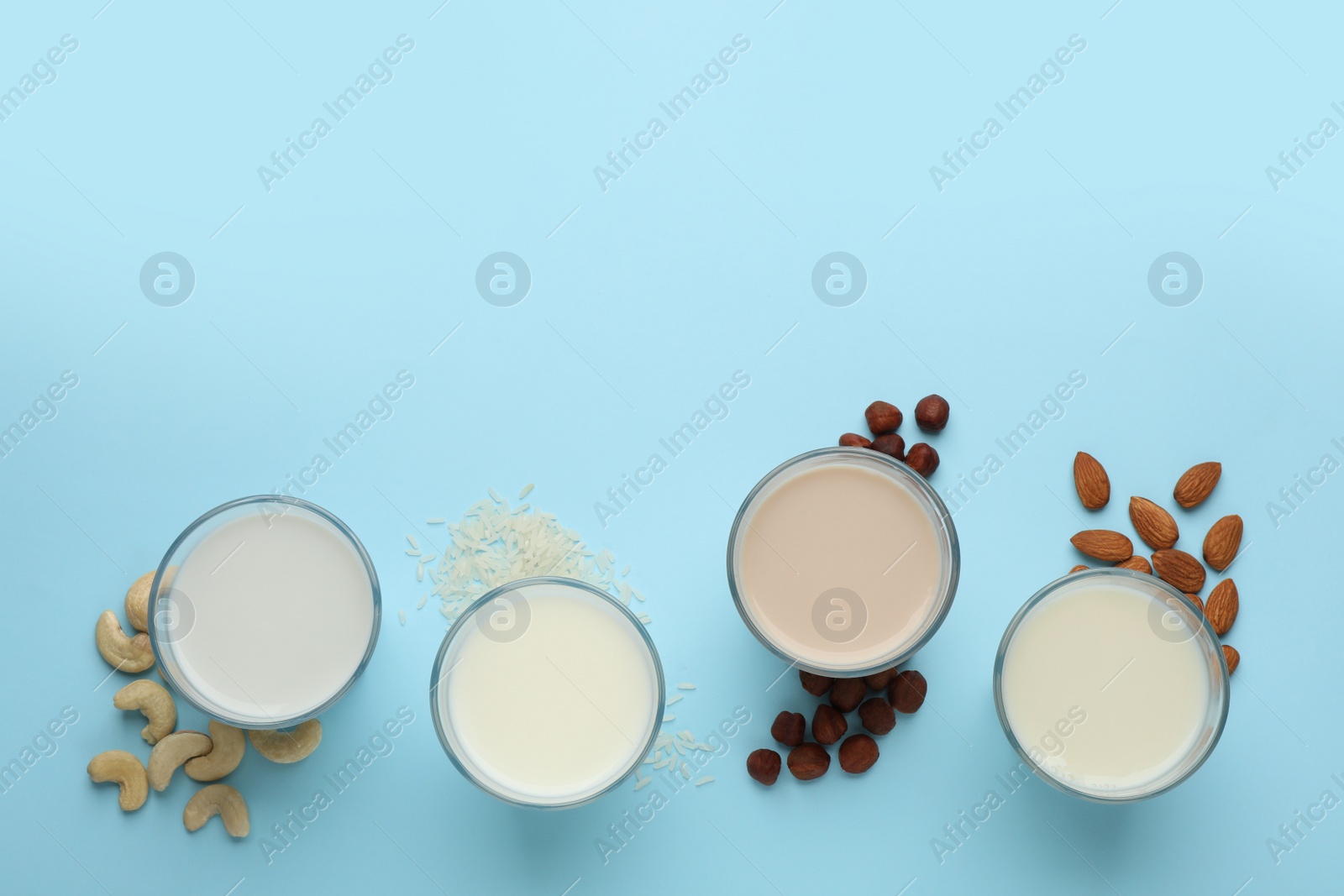 Photo of Different vegan milks, nuts and rice on light blue background, flat lay. Space for text