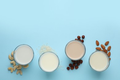 Different vegan milks, nuts and rice on light blue background, flat lay. Space for text