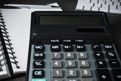 Calculator, notebook and pen on black table, closeup