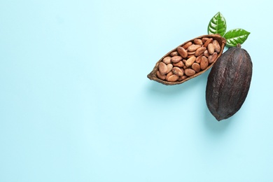 Cocoa pods and beans on light blue background, flat lay. Space for text