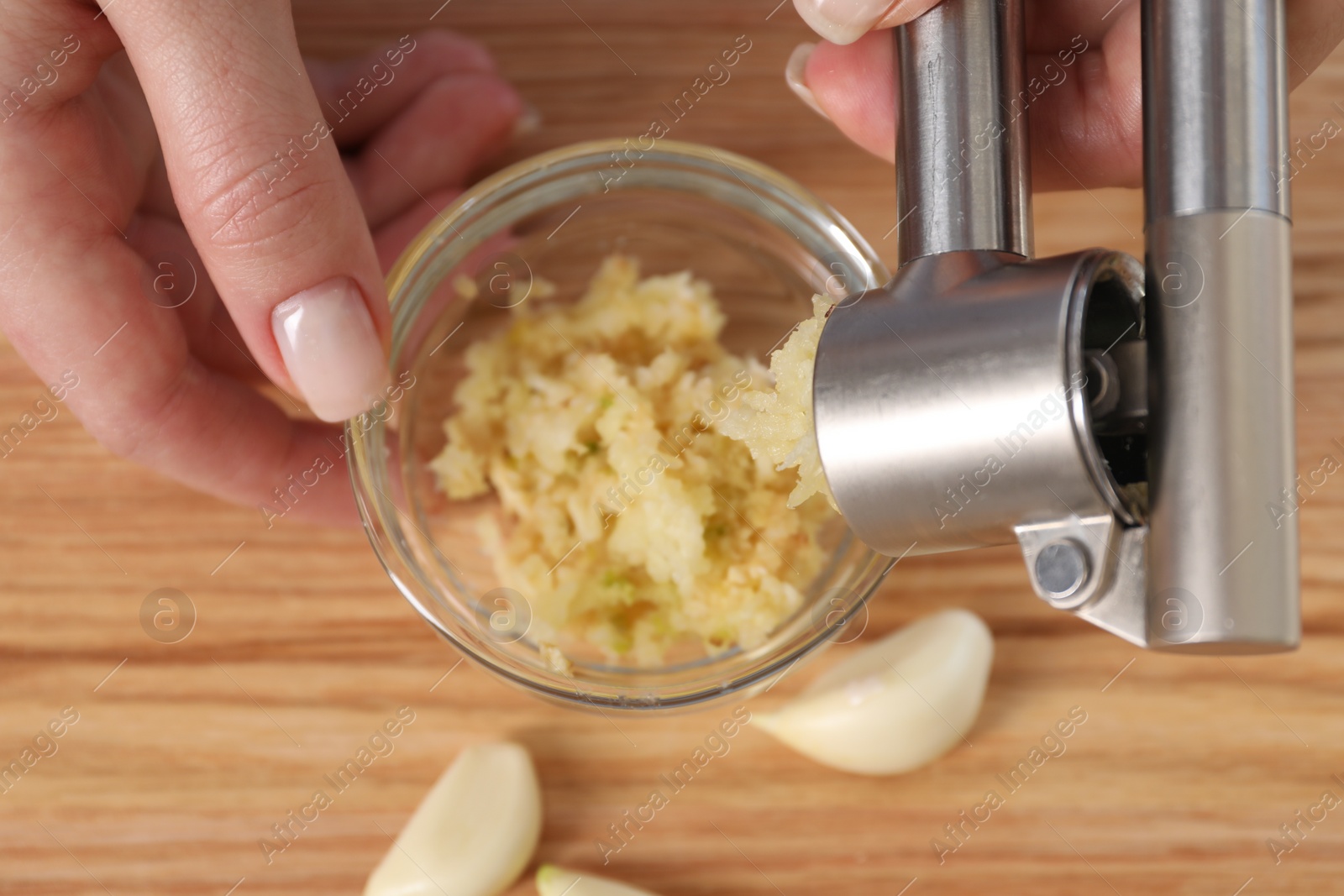 Photo of Woman squeezing garlic with press at wooden table, closeup