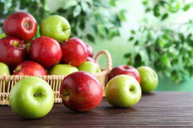 Photo of Juicy red and green apples in wicker tray on wooden table outdoors