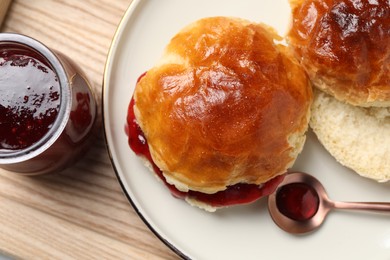 Photo of Plate with freshly baked soda water scones and cranberry jam on wooden table, closeup