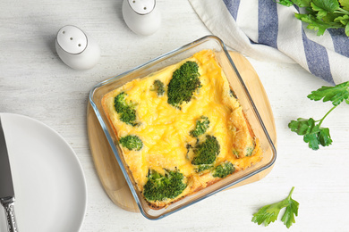 Tasty broccoli casserole in baking dish on white wooden table, flat lay