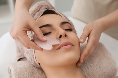 Young woman receiving facial massage with gua sha tool in beauty salon