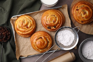 Photo of Delicious rolls with raisins and powdered sugar on table, flat lay. Sweet buns