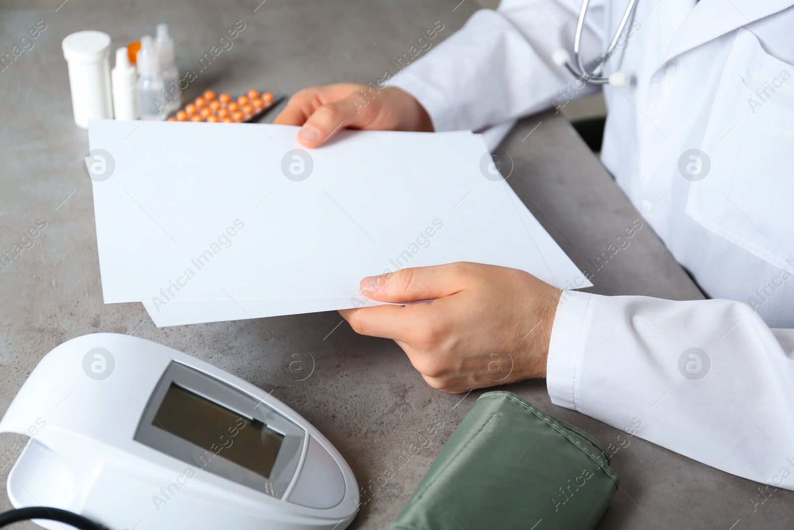 Photo of Doctor with papers and digital pressure meter at table, closeup with space for text. Medical objects