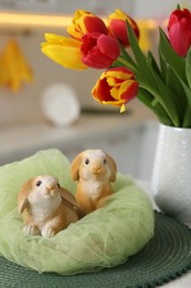 Photo of Easter decorations. Bouquet of tulips and bunny figures on table indoors, closeup