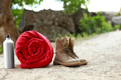 Photo of Rolled sleeping bag, boots and bottle outdoors. Space for text