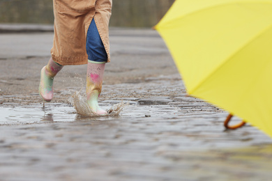 Photo of Woman in rubber boots jumping over puddle on rainy day, closeup