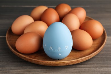 Photo of Plate with kitchen timer and chicken eggs on wooden table