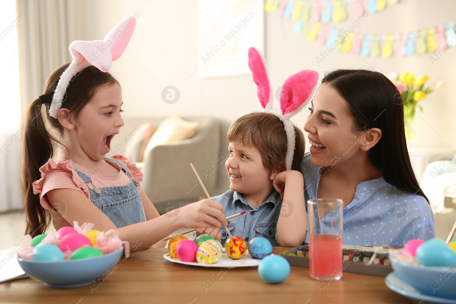 Photo of Happy mother with her children painting Easter eggs at table indoors
