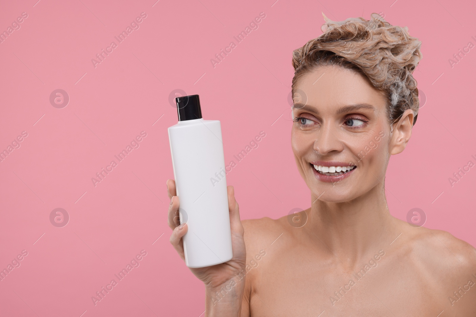 Photo of Beautiful happy woman with bottle washing hair on pink background. Space for text