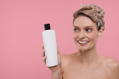 Beautiful happy woman with bottle washing hair on pink background. Space for text