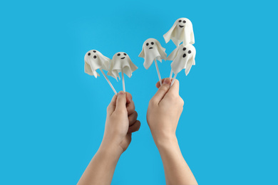 Photo of Woman with delicious ghost shaped cake pops on light blue background, closeup. Halloween celebration
