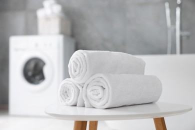 Rolled white towels on stool in bathroom