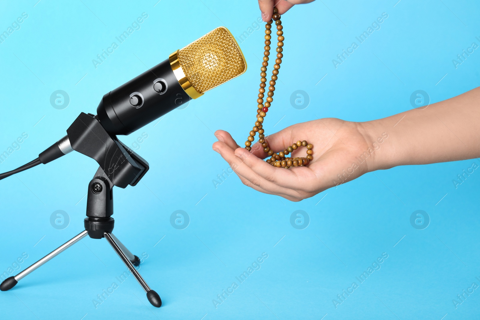 Photo of Woman making ASMR sounds with microphone and beads on light blue background, closeup