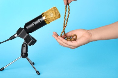 Photo of Woman making ASMR sounds with microphone and beads on light blue background, closeup