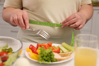 Overweight woman measuring waist while having meal at home, closeup