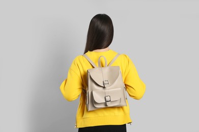 Young woman with stylish leather backpack on grey background, back view