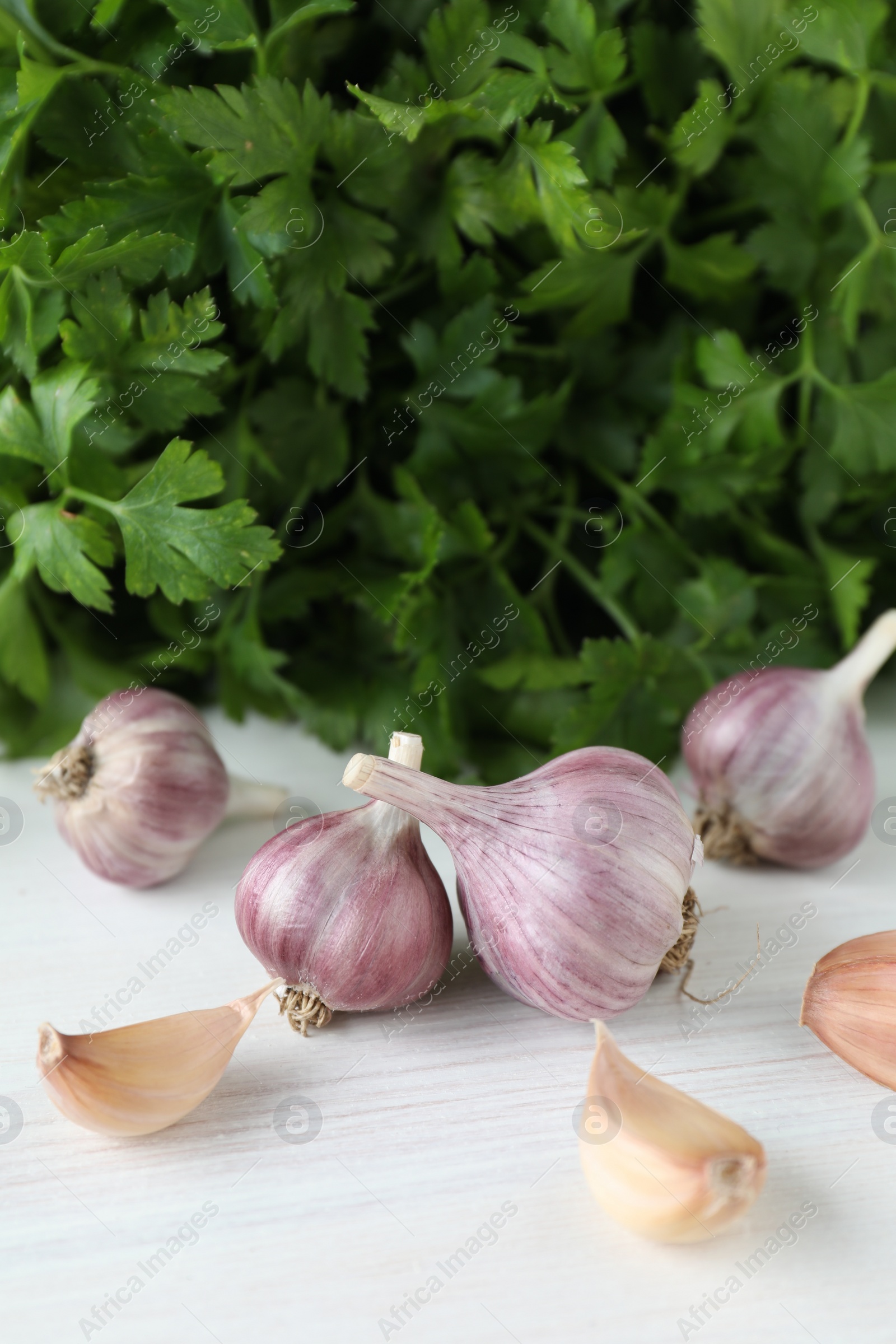 Photo of Fresh raw garlic and parsley on white wooden table, closeup