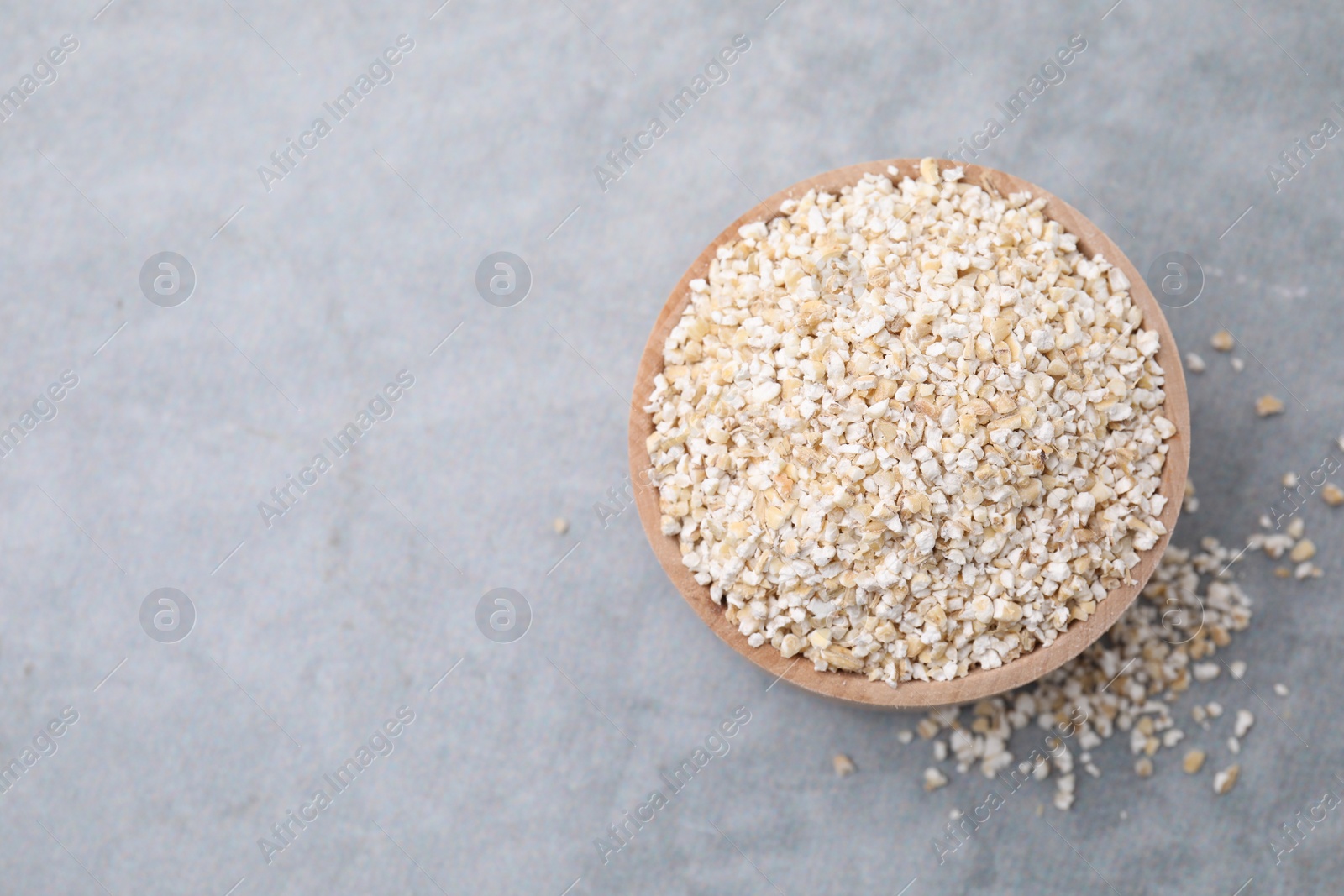 Photo of Raw barley groats in bowl on grey table, top view. Space for text
