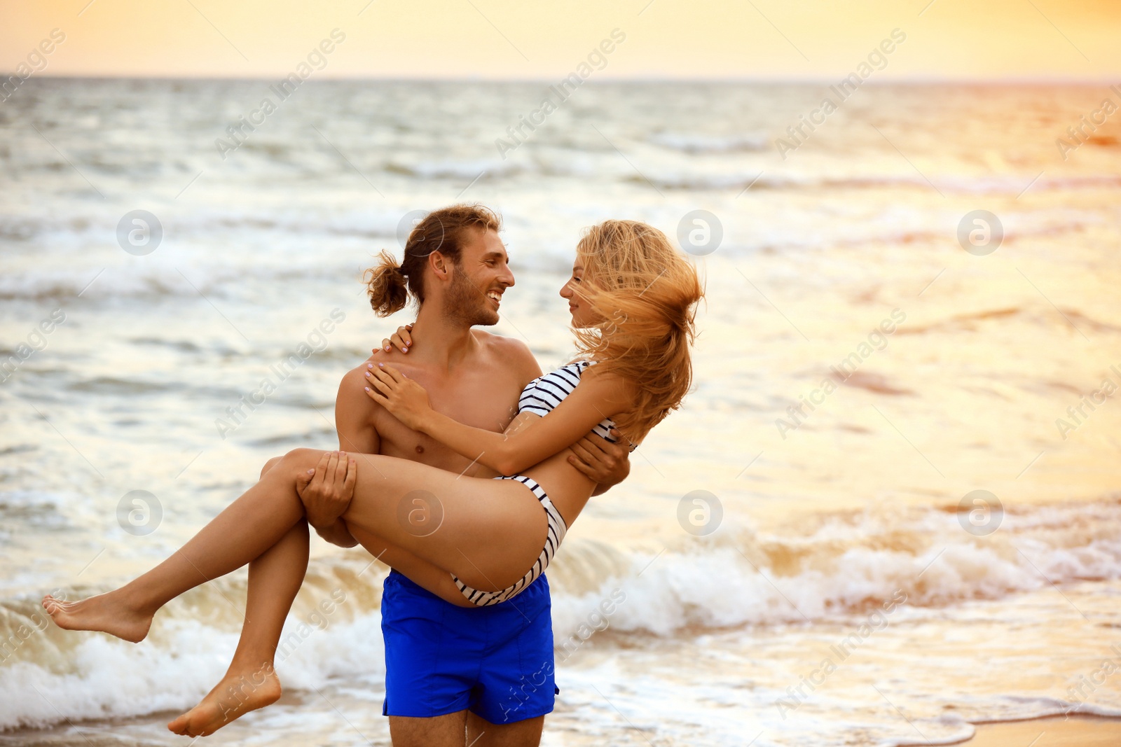 Photo of Young woman in bikini and her boyfriend having fun on beach at sunset. Lovely couple