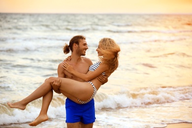 Young woman in bikini and her boyfriend having fun on beach at sunset. Lovely couple