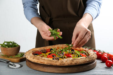 Photo of Woman adding arugula to vegetable pizza at table, closeup