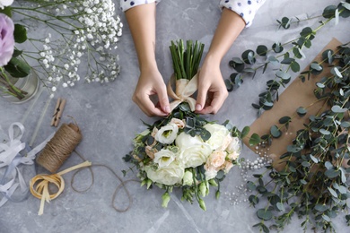 Florist tieing bow on beautiful wedding bouquet at light grey marble table, top view