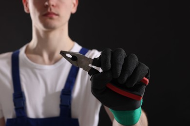 Photo of Young man holding pliers on black background, closeup