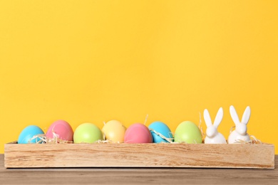 Photo of Wooden stand with ceramic bunnies and Easter eggs on table against color background