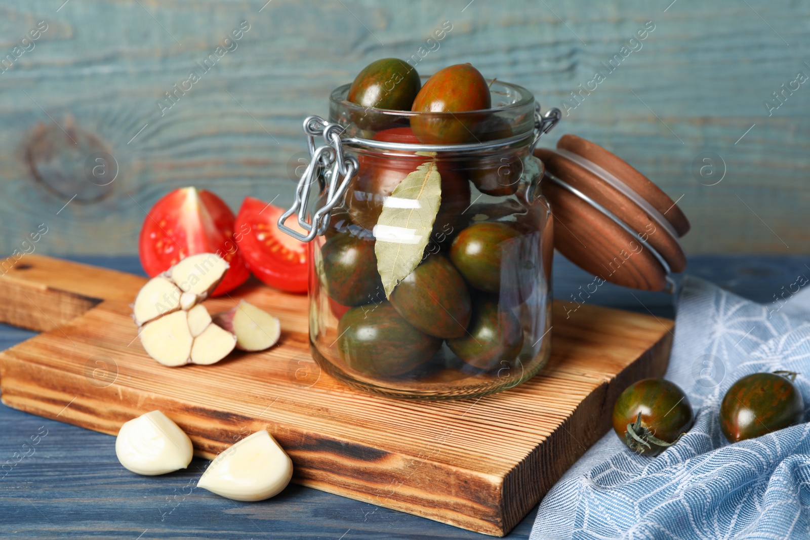 Photo of Pickling jar with fresh ripe tomatoes on blue wooden table