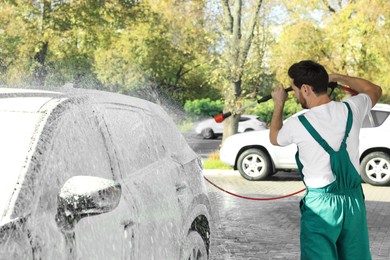 Worker washing auto with high pressure water jet at outdoor car wash