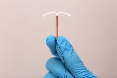 Photo of Doctor holding T-shaped intrauterine birth control device on grey background, closeup