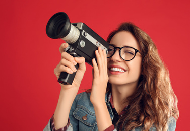 Beautiful young woman with vintage video camera on red background