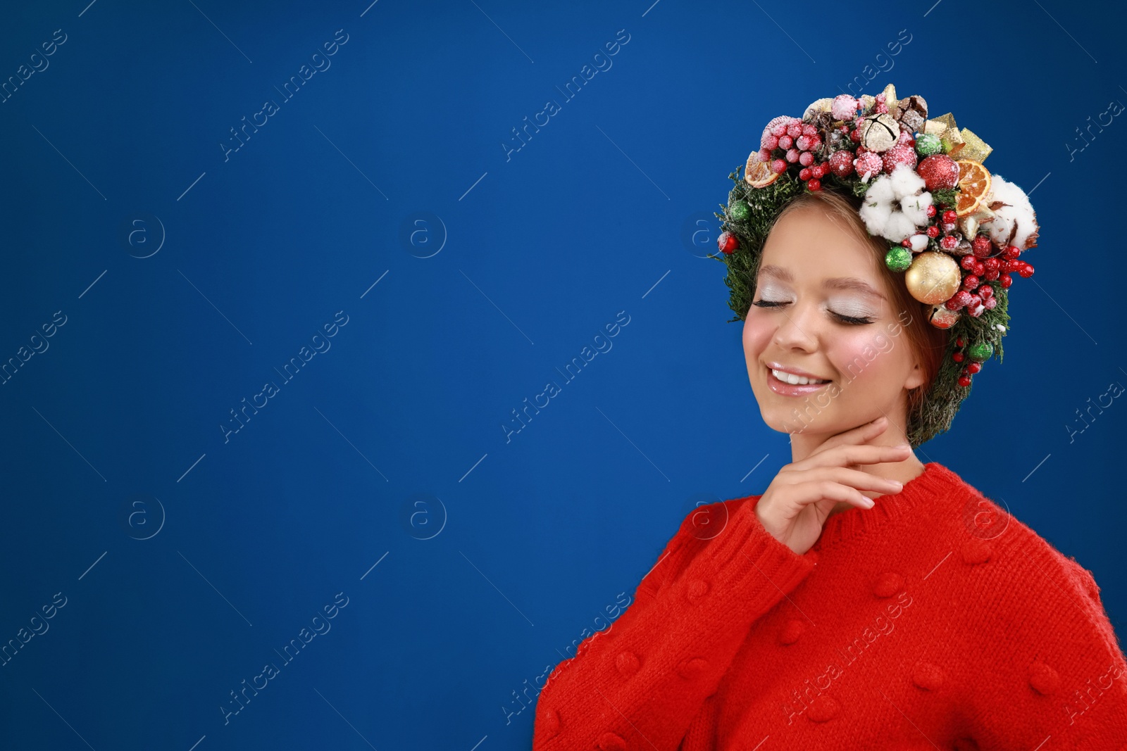 Photo of Beautiful young woman wearing Christmas wreath on blue background. Space for text