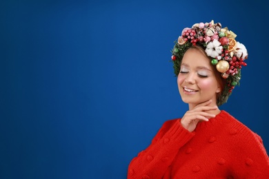 Photo of Beautiful young woman wearing Christmas wreath on blue background. Space for text