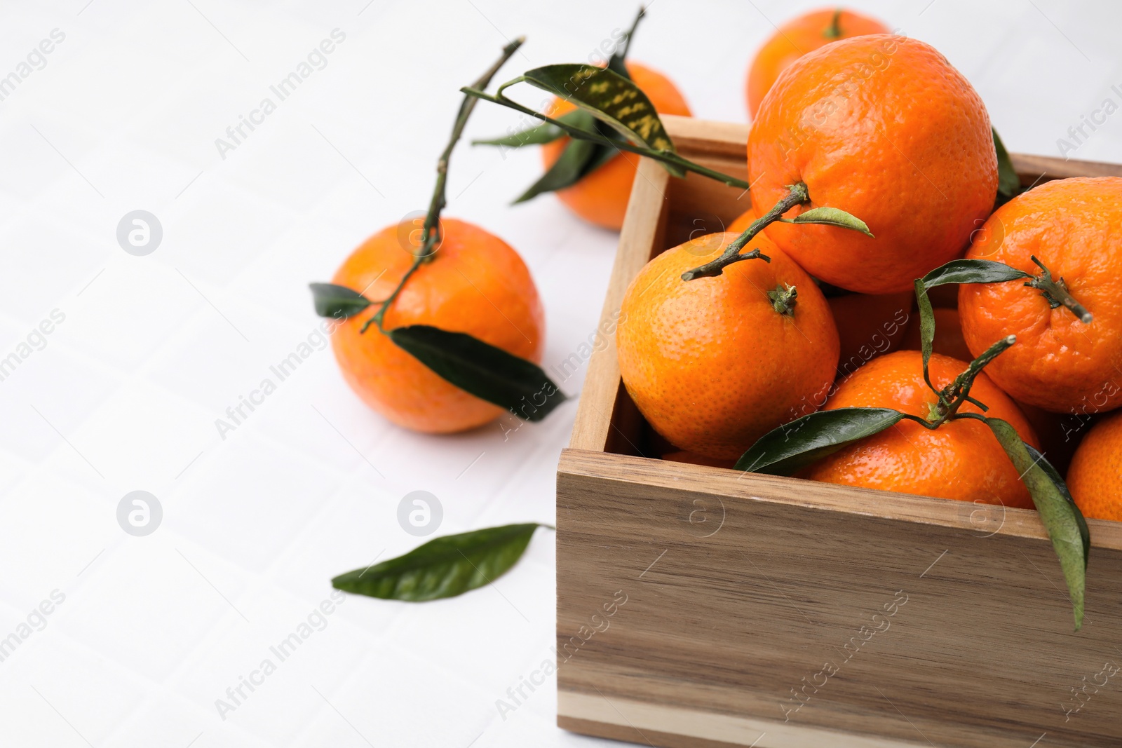 Photo of Wooden crate with fresh ripe tangerines and leaves on white table, closeup. Space for text