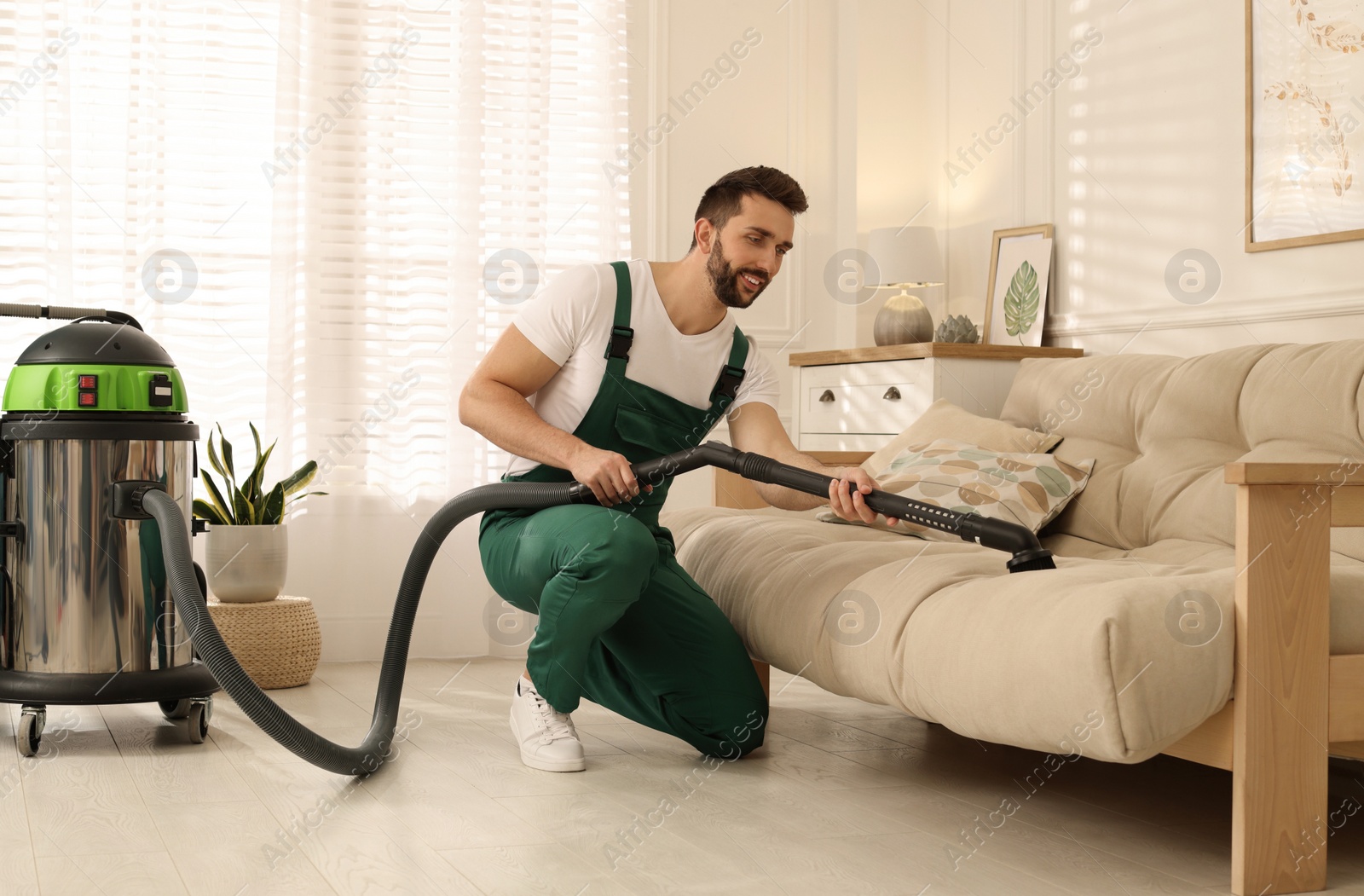 Photo of Professional janitor vacuuming sofa in living room