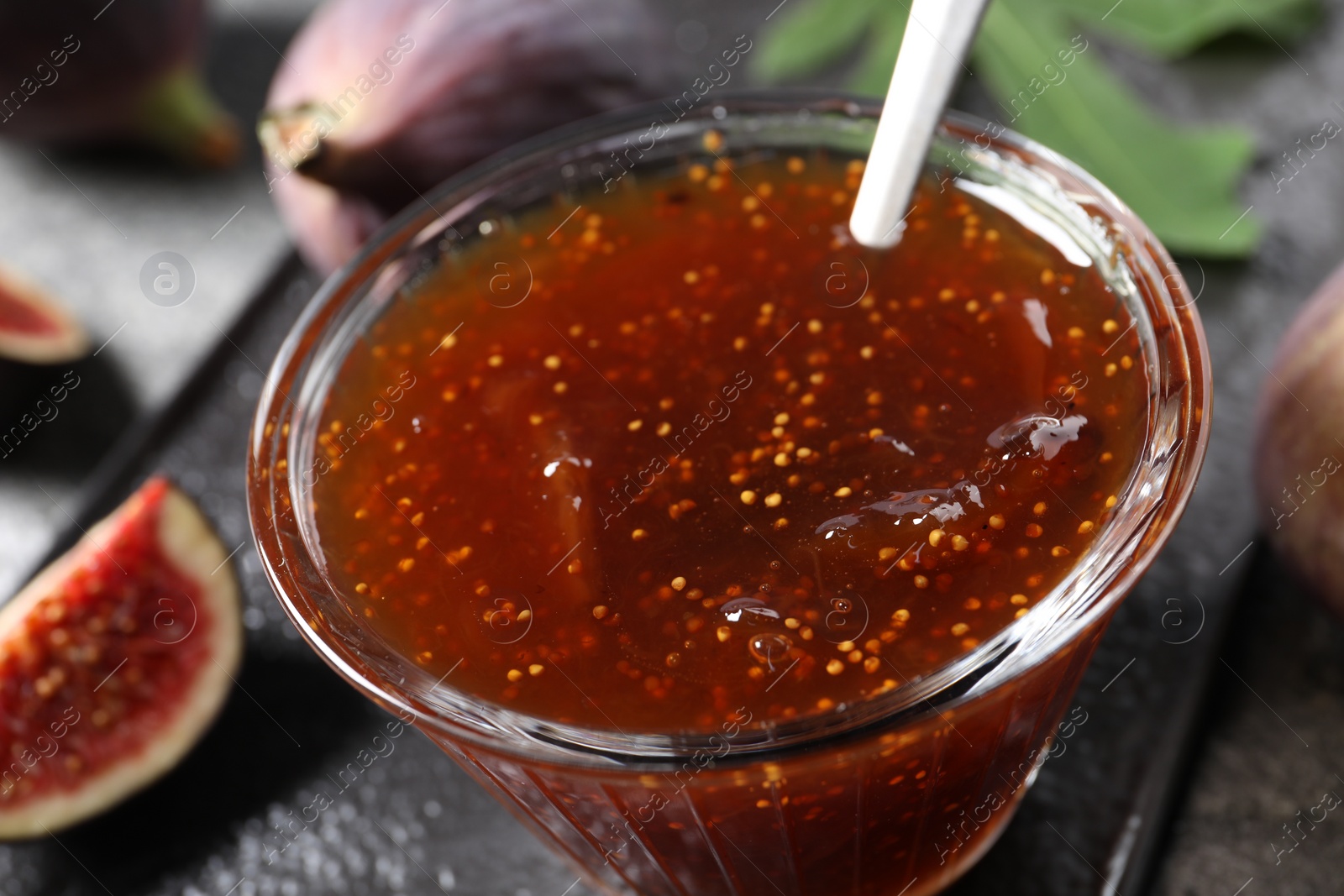 Photo of Glass bowl with tasty fig jam on table, closeup
