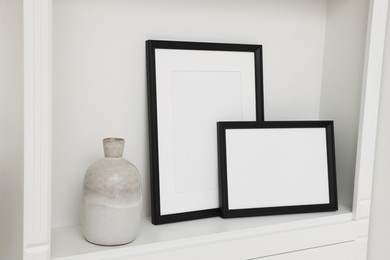 Photo of Blank frames and ceramic vase on shelving unit indoors