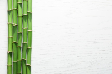 Photo of Green bamboo stems and space for text on wooden background, top view