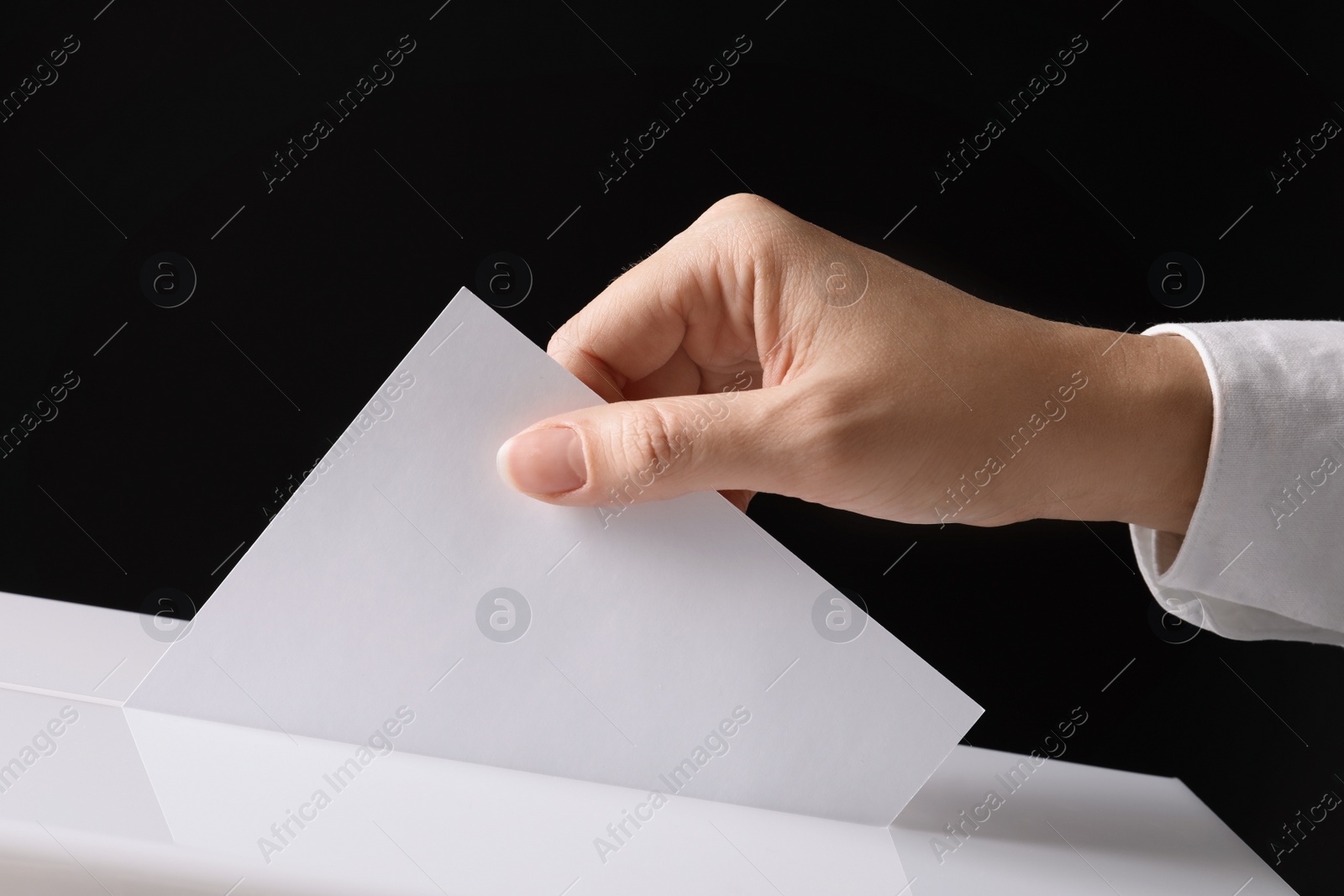 Photo of Woman putting her vote into ballot box on black background, closeup