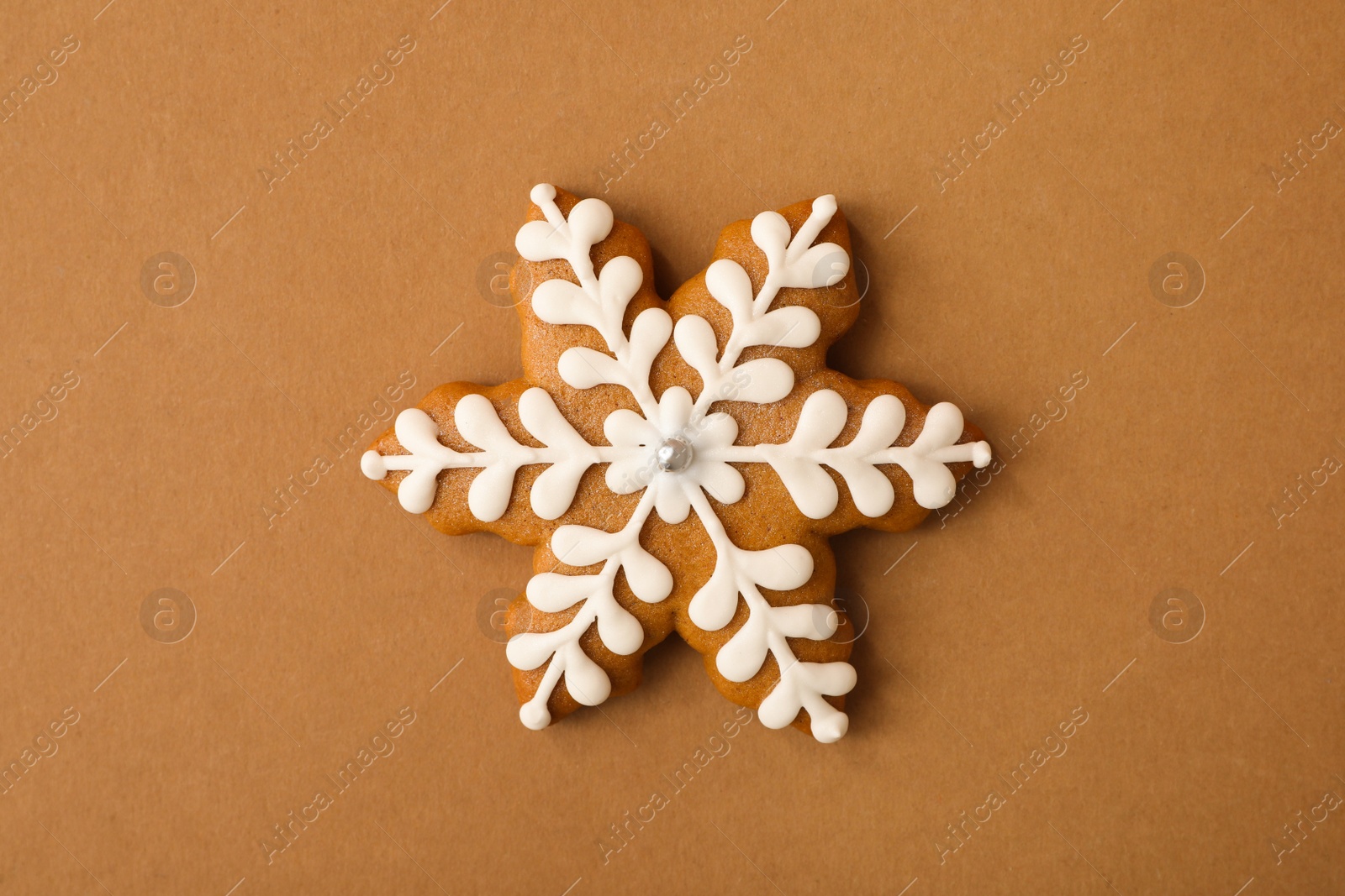 Photo of Christmas snowflake shaped gingerbread cookie on brown background, top view