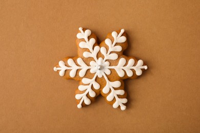 Photo of Christmas snowflake shaped gingerbread cookie on brown background, top view