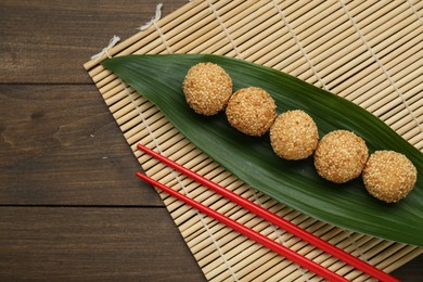 Photo of Delicious sesame balls, green banana leaf and chopsticks on wooden table, flat lay. Space for text